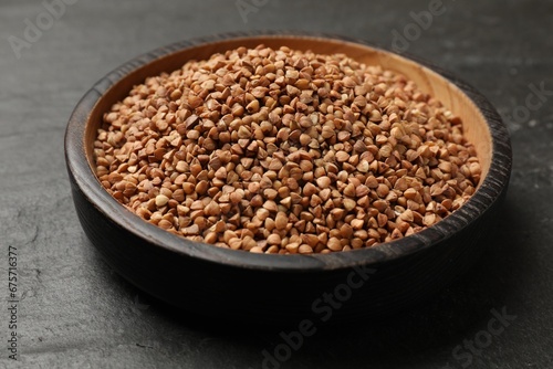 Bowl with dry buckwheat on black table, closeup