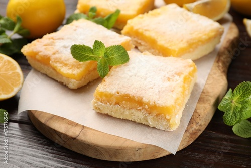 Tasty lemon bars with powdered sugar and mint on wooden table, closeup