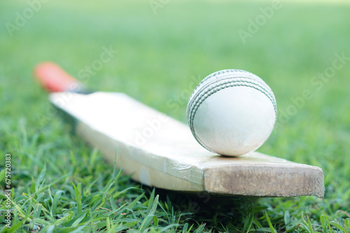 White cricket ball on wooden bat. Concept, sport equipment. Competitive sport. A cricket ball is made with a core of cork, covered by a leather case with a slightly raised sewn seam              