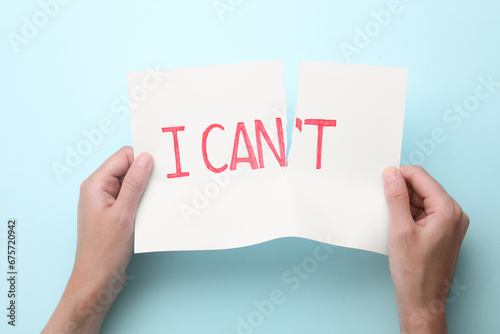 Motivation concept. Woman making phrase I Can from I Can't by tearing paper on light blue background, top view