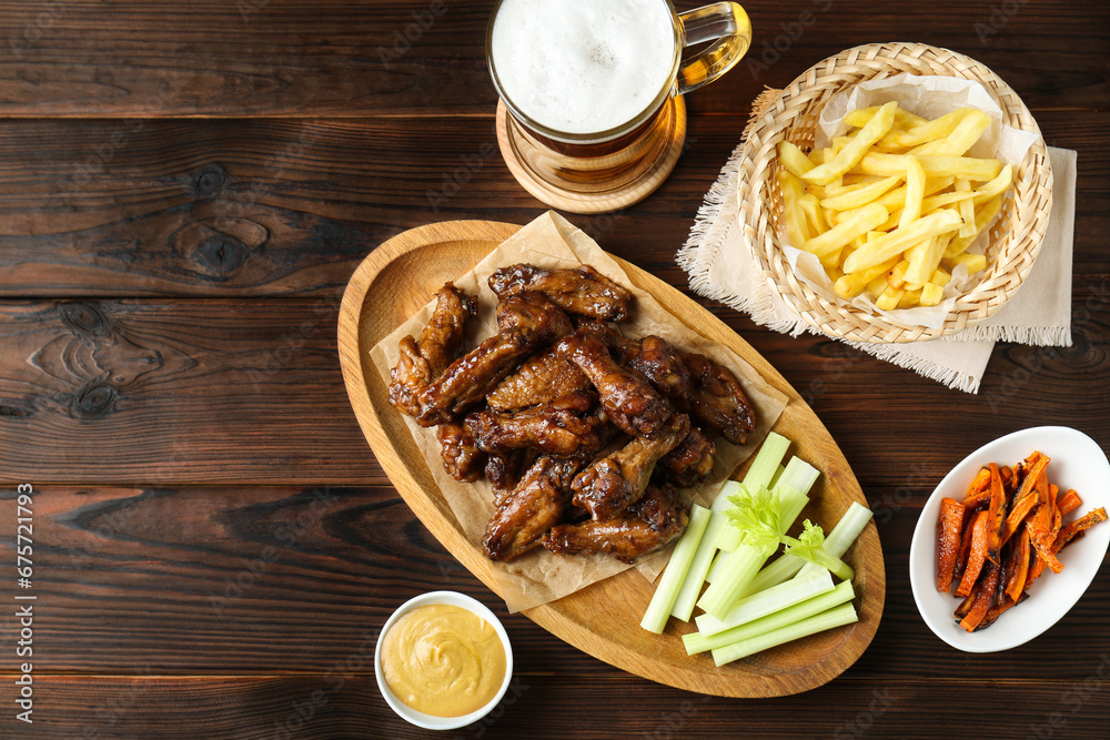 Delicious chicken wings served with beer on wooden table, flat lay