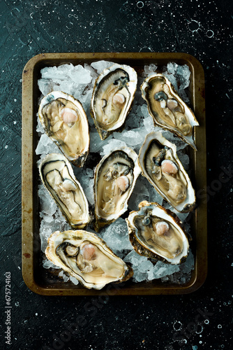 Fresh oysters with lemon laid out on ice in a metal tray. On a black stone background. Top view.