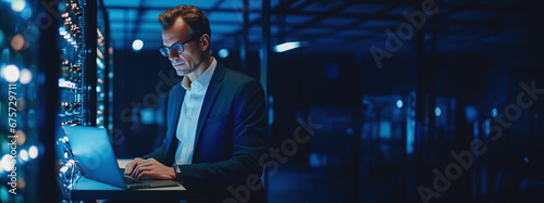 Man IT Engineers repairs technical problem and adjusts server room with laptop notebook, blue color light. Banner photo digital programmer job