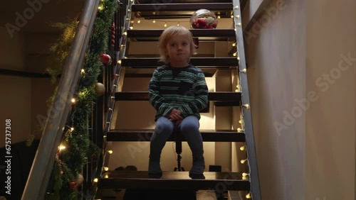 Little boy sitting on stairs decorated for Christmas or New Year and looking at police lights and siren. Concept of Crime on winter holidays, theft, burglar in house and protection.