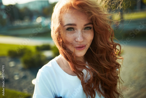 Portraits of a charming red-haired girl with a cute face. Girl posing for the camera in the city center. She has a wonderful mood and a lovely smile