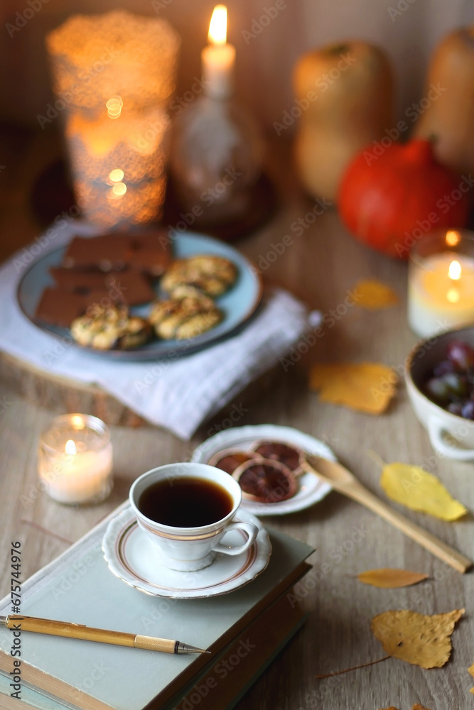 Cup of tea or coffee, plate with desserts, dried oranges, bowl of grapes, scented candles, vintage books, pumpkins and autumn leaves on the table. Autumnal hygge. Selective focus. Cup of tea or coffee, plate with desserts, dried oranges, bowl of grapes, scented candles, vintage books, pumpkins and autumn leaves on the table. Autumnal hygge. Selective focus.