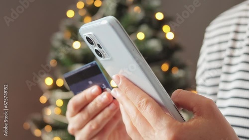 During Christmas season woman using her smartphone to shop for holiday decorations online holding credit card entering data for paying while staying cozy indoors in winter. photo