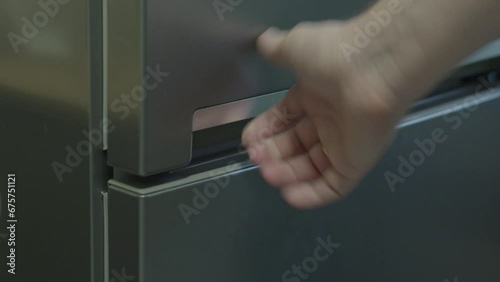 A man's hand opens and closes the doors of a gray refrigerator photo