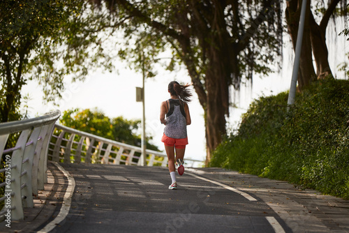 rear view of young asian woman jogging running exercising outdoors in park