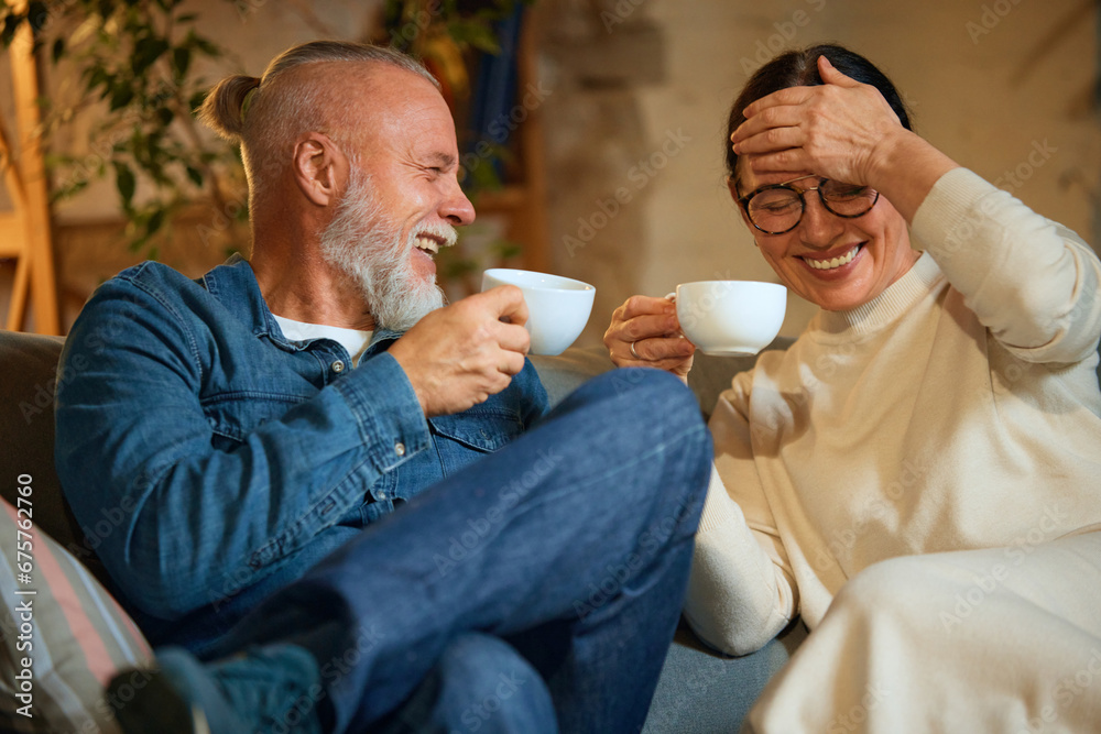 Joyful and happy mature couple sitting in living room and remember their youth, past over cup of tea, coffee at home.