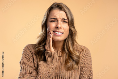 Portrait upset young woman touching face, toothache, looking at camera isolated on beige background © Maria Vitkovska