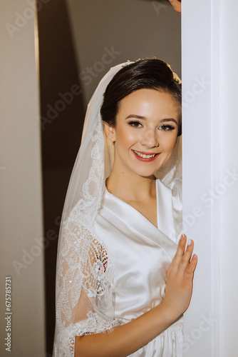 The bride in a silk suit with a veil poses in her room. Morning of the bride. Preparation. Wedding photography