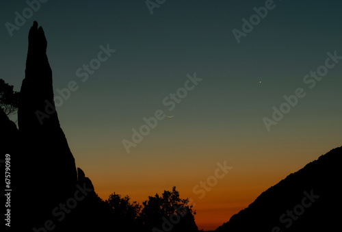 La luna crescente brilla nel cielo al tramonto, accompagnata dal gigante gassoso Giove. La scena è resa ancora più suggestiva dalle nuvole rosa e arancioni che si stagliano sullo sfondo.