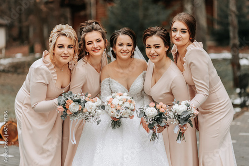 A brunette bride in a white elegant dress and her friends in gray dresses pose with bouquets. Wedding portrait in nature, wedding photo in light colors. photo
