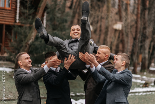 The groom and his friends are dressed in suits, fooling around in nature during a photo shoot. A group of men. Wedding in nature