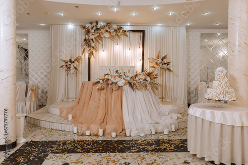 The wedding table of the bride and groom, decorated with flowers, dried ears of corn and white tulle, is made in nude color. Flowers on stands. Wedding details. light