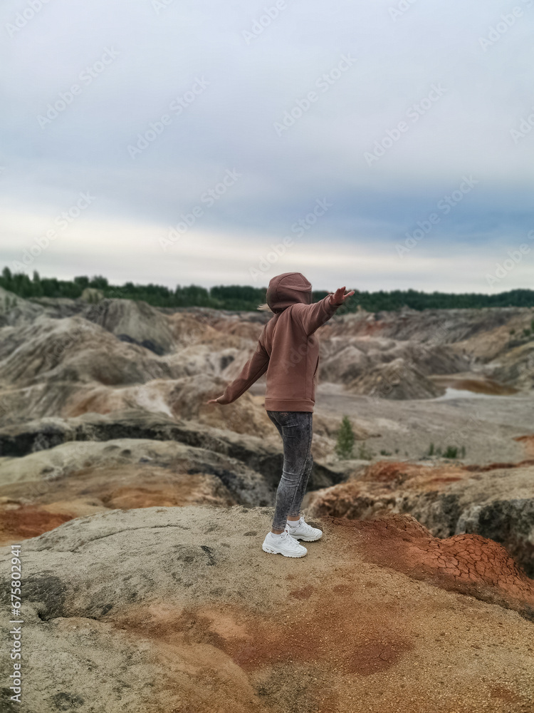 A girl on the background of the Ural Mars. An extraordinarily beautiful summer landscape with red lakes, colorful slopes and forest. Natural landscape, impressive sky.