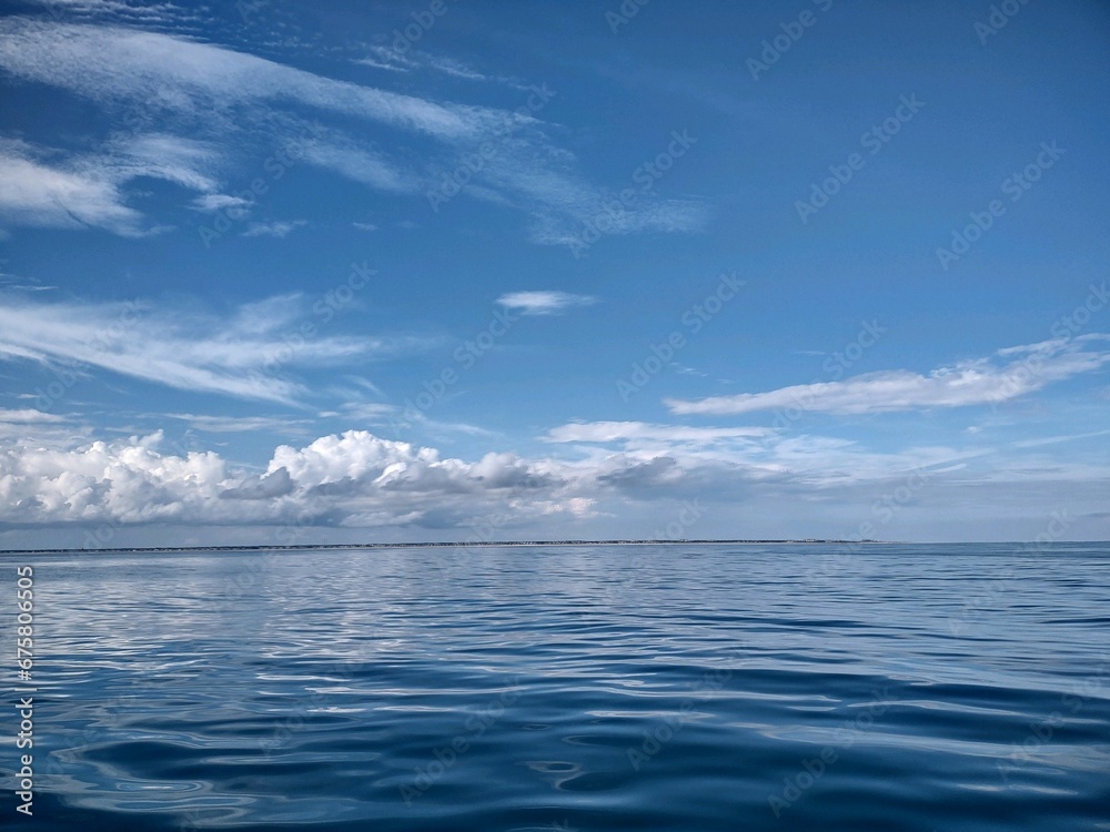 Tranquil scene of an ocean in pastel blue hues with white fluffy clouds in the sky