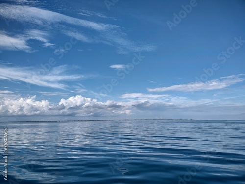 Tranquil scene of an ocean in pastel blue hues with white fluffy clouds in the sky © Wirestock