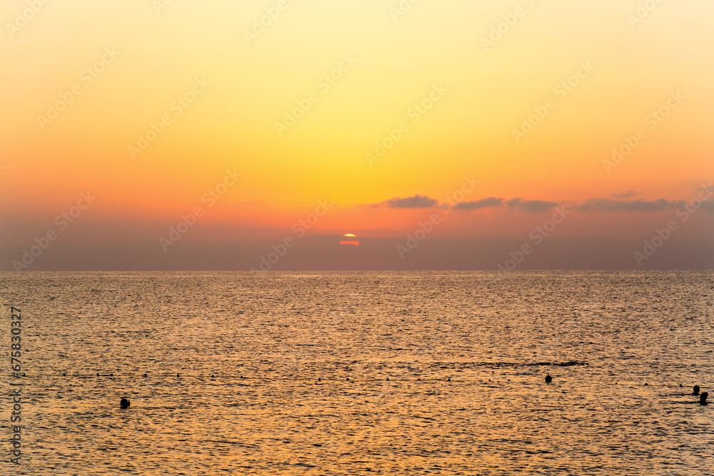Sunset over the sea with rare floating people the water.