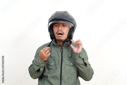 Stressed asian man standing while wearing helmet. Isolated on white background