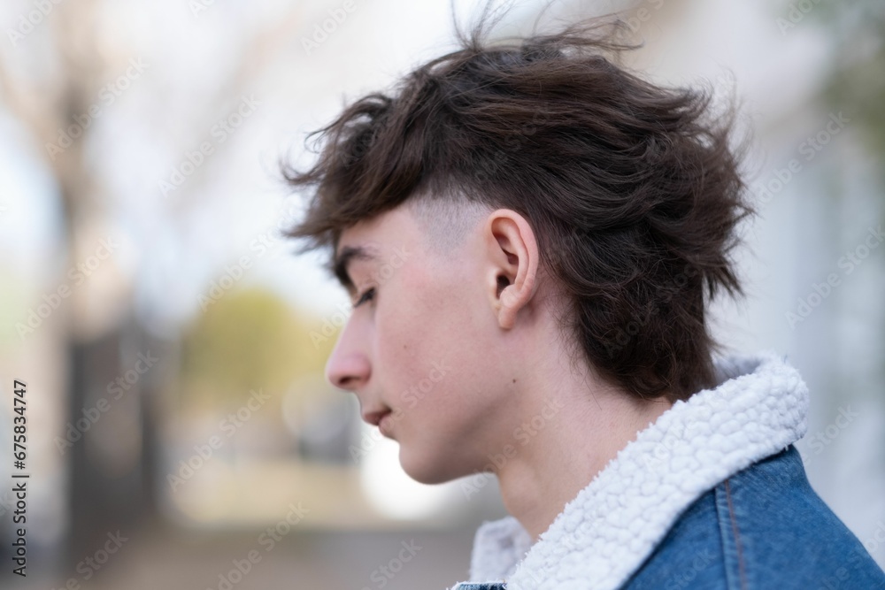 Young male with a trendy haircut standing in a city street in a denim jacket Young male with a trendy haircut standing in a city street in a denim jacket