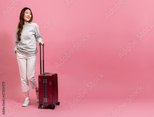Beautiful asian female passenger in sweater, jeans, and luggage. Portrait of a smiling girl with luggage in full length size. Winter lifestyle and travel concept