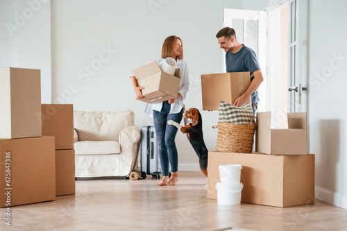Two boxes in hands. Young couple with dog are moving to new home photo