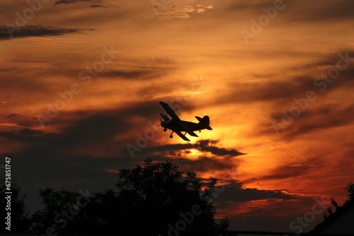 Plane silhouette is seen flying above a stunning sunset landscape