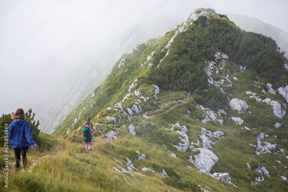 Fototapeta premium People trekking up a steep incline towards a range of misty mountains in Triglav National Park