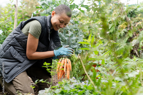 Smiling woman holding bunch of carrots in urban garden photo
