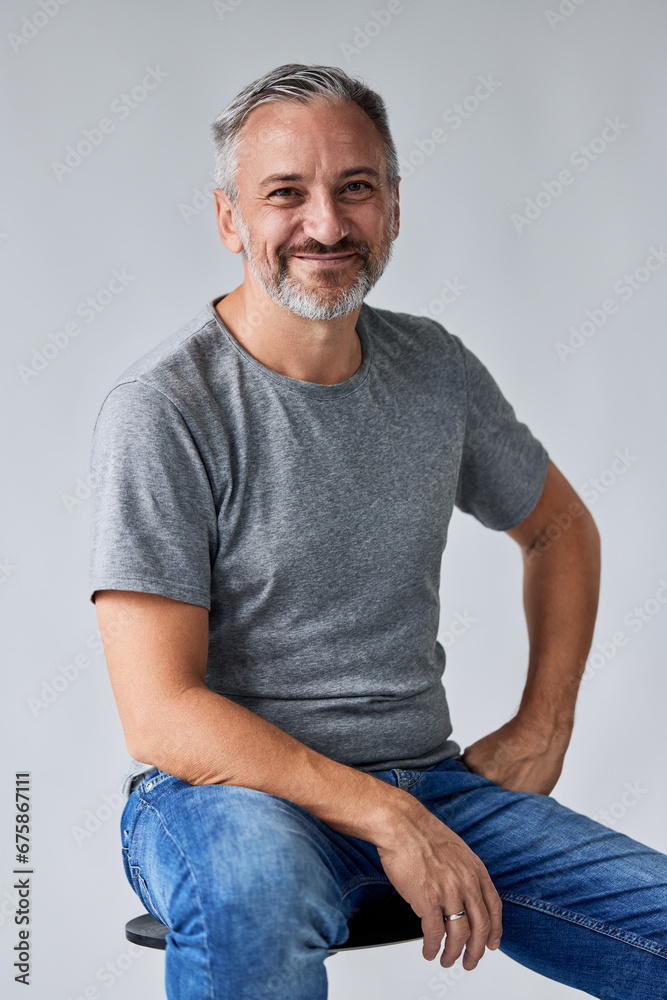A portrait of a happy mature man, sitting on the chair and posing for the camera on the white background.
