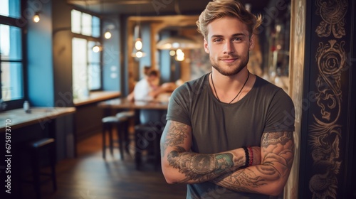 A handsome young man with tattoos on his body stands smiling looking at the camera. Freelance designer