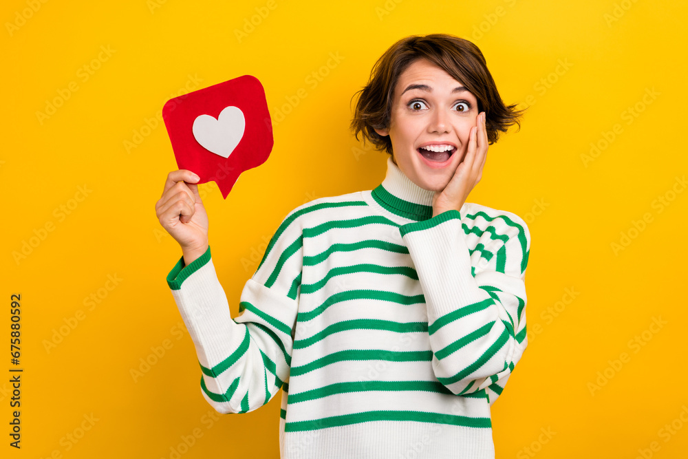 Photo of sweet shocked lady wear striped pullover arm hand cheek cheekbone rising heart like card isolated yellow color background Photo of sweet shocked lady wear striped pullover arm hand cheek cheekbone rising heart like card isolated yellow color background