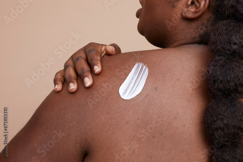 Studio shot of young woman applying moisturizer on back