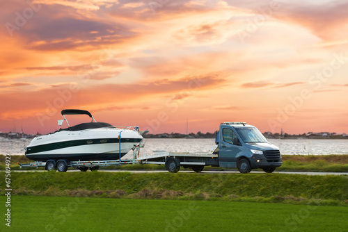 Luxury Boat Journey on the Road at Sunset. Modern motorboat delivery on the driveway. Sunset sky. photo