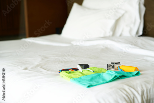 travel gears ,action camera ,handle stick,sunglasses and swimming suit on bed ,top view