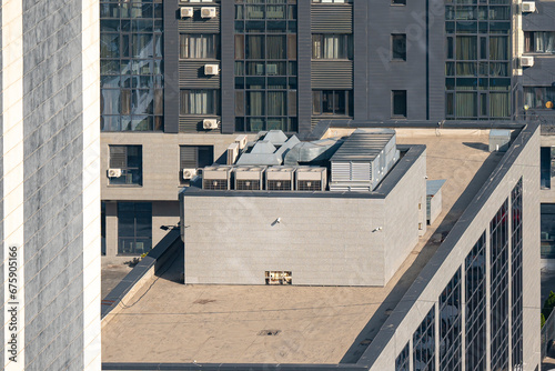 A flat roof with air conditioning and an air vent system at the top. Exterior of a modern office building on the background of the facade of a residential building