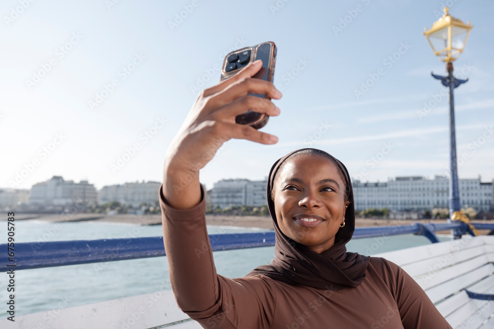 Muslim woman taking selfie with sea view on sunny day
