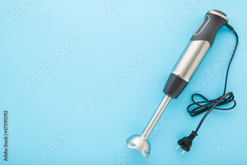 New hand blender with black wire on blue table background. Pastel color. Closeup. Kitchen electrical appliance for fruit, vegetable, meat or other food blending. Empty place for text. Top down view. photo