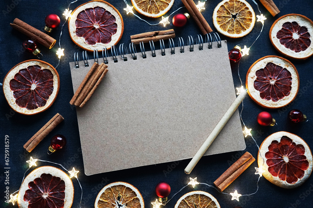 Notepad with pen next to dry fruit slices, Christmas tree decorations, cinnamon sticks on a dark background Notepad with pen next to dry fruit slices, Christmas tree decorations, cinnamon sticks on a dark background
