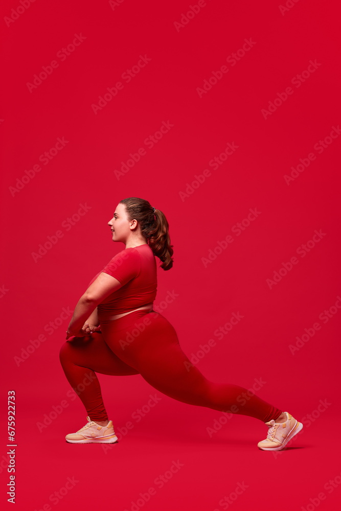 Plus size model. Young woman with fat, overweigh body training, doing exercises against red studio background. Concept of sport, body-positivity, weight loss, body, health care. Plus size model. Young woman with fat, overweigh body training, doing exercises against red studio background. Concept of sport, body-positivity, weight loss, body, health care.