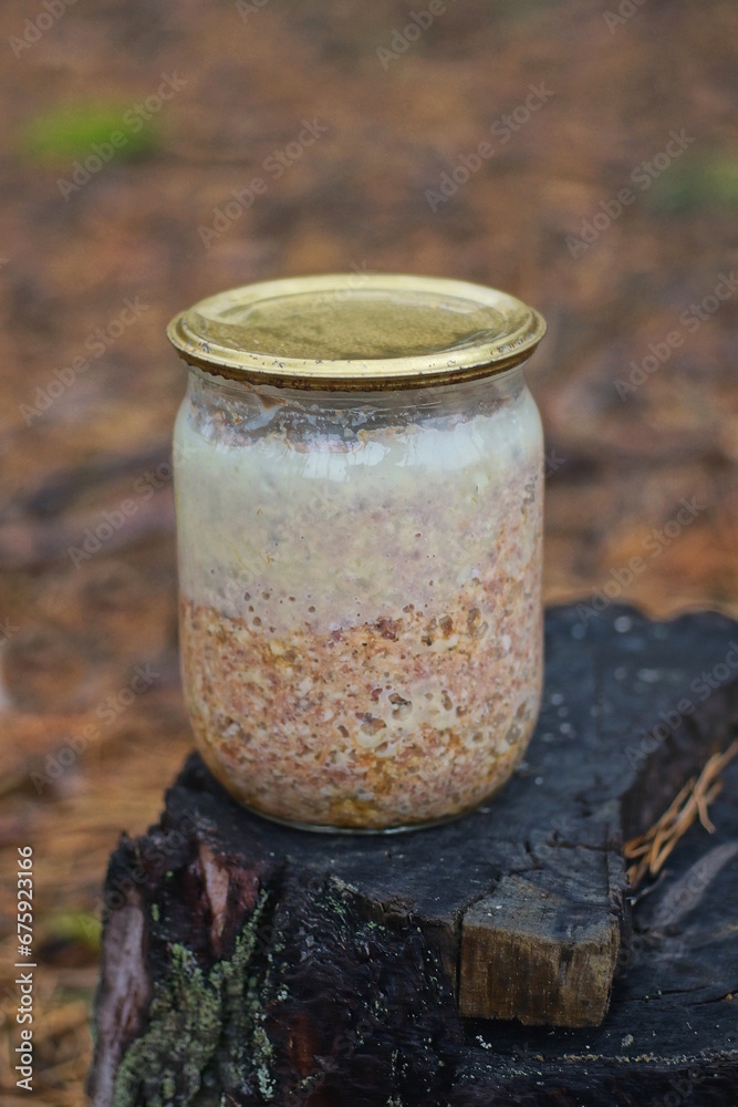 one glass jar with brown chicken stew standing on a stump on the street one glass jar with brown chicken stew standing on a stump on the street
