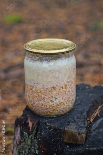 one glass jar with brown chicken stew standing on a stump on the street