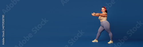 Fat, overweigh young woman training with elastic bands, fitness expanders against blue studio background. Concept of sport, body-positivity, weight loss, body and health care. Copy space for ad photo