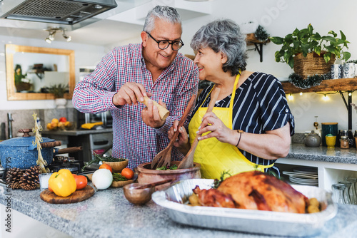 Latin senior couple cooking a turkey meat together for Christmas dinner at home in Mexico Latin America, hispanic people preparing food in holidays photo