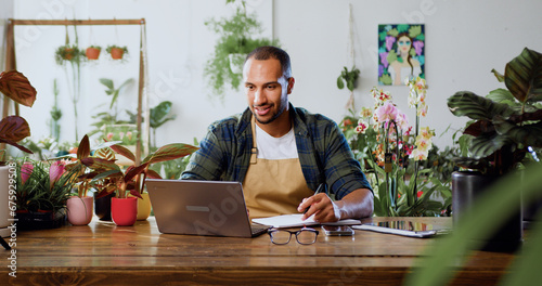 Caucasian man florist using laptop, typing and taking inventory in Plant Store. Botanist working, small business owner. Florist working on computer at workplace.