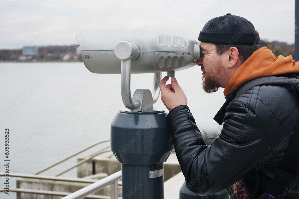 A man in a docker's cap looks at the binocular viewer on the sea promenade