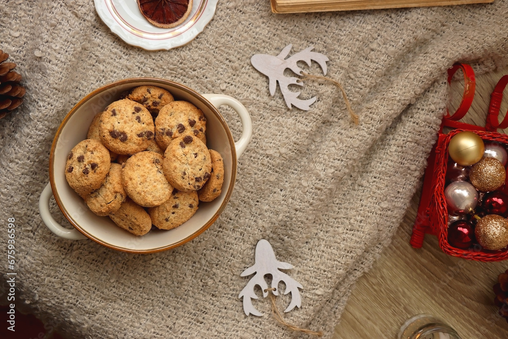 Bowl of cookies, cup of tea, dry oranges, pine cones, book, reading glasses and various neutral Christmas decorations on soft beige blanket. Cozy Christmas hygge. Top view. Bowl of cookies, cup of tea, dry oranges, pine cones, book, reading glasses and various neutral Christmas decorations on soft beige blanket. Cozy Christmas hygge. Top view.