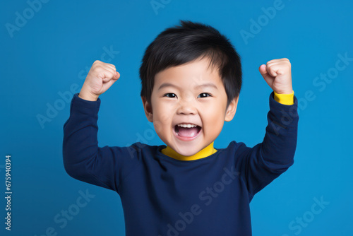 Asian Boy in Blue Sweater Raises Fist on Blue Background